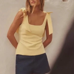 Gul ärmlös topp med knytband - Snygg gul topp med breda axelband som knyts i rosetter. Den är ärmlös och har en figurnära passform. Om någon vill byta denna M mot en L, skriv!! Annars säljer jag den för 300 som lägst💛