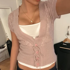 Rosa kortärmad kofta med knytning - Säljer en söt rosa kofta med korta ärmar och knytning framtill. Koftan har fina stickade detaljer och knappar i matchande färg. Perfekt för en avslappnad och stilren look.