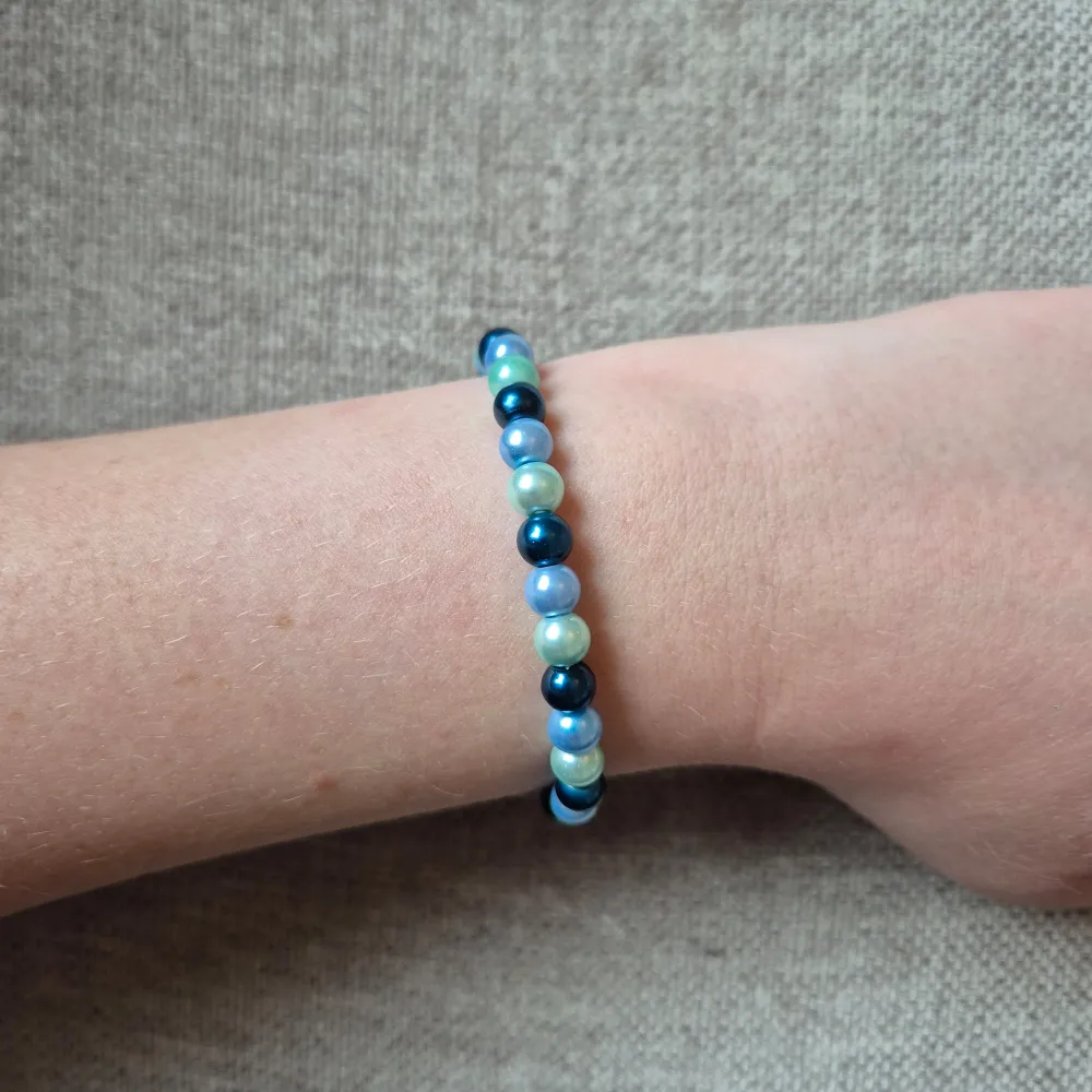 Snyggt armband med pärlor i blå, gröna och ljusblå nyanser. Perfekt accessoar för att ge en färgklick till din outfit. Elastiskt band för enkel passform.. Asusteet.