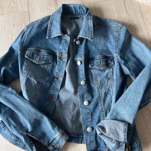 Jeansjacka från Vero Moda - Snygg jeansjacka från Vero Moda i klassisk blå denim. Jackan har en normal passform med långa ärmar och knappar framtill. Två bröstfickor med knappdetaljer ger en cool touch. Perfekt för vår och sommar!🩷