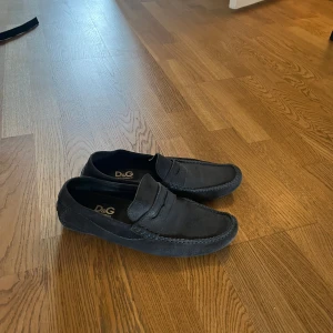 Svarta mockaloafers från D&G - Snygga  loafers från Dolce & Gabbana i mjuk mocka. Skorna har klassisk penny loafer-design med rund tå och diskret söm längs kanterna. Sulan har D&G-logga i gummi för extra grepp och stil.