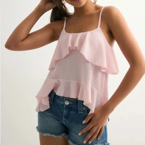Ljusrosa volangig linnetopp - Supersöt ljusrosa linnetopp med tunna axelband och dubbla volanger både fram och bak. Toppen har en luftig och flowy passform, perfekt för varma dagar.