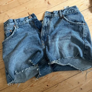 Blå jeansshorts med fransig kant - Säljer ett par klassiska blå jeansshorts med rå, fransig kant och femficksmodell. Shortsen har normal passform och är perfekta för varma dagar. Snyggt slitna detaljer och tidlös denim-look som alltid funkar.