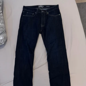 Mörkblå jeansbyxor Dressman - Snygga mörkblå jeansbyxor från dressman med klassisk femficksdesign och kontrastsömmar. Perfekta till vardags och har en rak passform som funkar till det mesta. Stängs med dragkedja och knapp. Storlek W32/L30