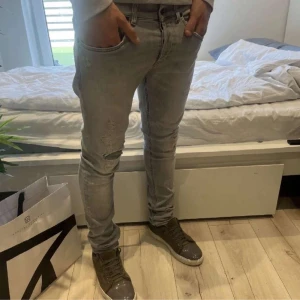 Grå skinny jeans med slitningar - Säljer ett par ljusgrå skinny jeans med snygga slitningar och trasiga detaljer på benen. Jeansen har klassisk femficksdesign och smal passform som sitter tight hela vägen ner. Perfekta för dig som gillar en trendig och avslappnad streetstil.