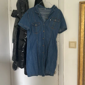 Kort jeansklänning med knappar - Snygg kort jeansklänning i blå denim med korta ärmar och knappar hela vägen framtill. Två bröstfickor med lock och krage ger en cool och avslappnad look. Perfekt för dig som gillar en casual stil med edge. 💌köparen står för frakten!