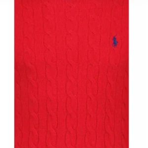 Röd kabelstickad tröja från Polo Ralph Lauren - Kabelstickad röd tröja från Polo Ralph Lauren med rund halsringning och blå broderad logga på bröstet. Långärmad modell med ribbade muddar och nederkant. Perfekt för dig som vill ha en klassisk och snygg look.