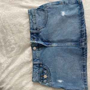 Lågmidjad jeanskjol från Zalando - Snygg ljusblå jeanskjol köpt på Zalando med klassiska fickor fram och bak, samt små slitna detaljer. Kjolen har dragkedja och knapp framtill och är i en kort modell (minikjol)