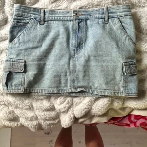 Ljusblå jeanskjol från Pull&Bear - Säljer en ljusblå jeanskjol från Pull&Bear med cargofickor på sidorna och bälteshällor. Är typ en 36-38 i storlek. 