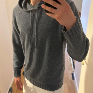 Stickad hoodie - Säljer en ljusblå stickad hoodie gjord av ull från dressmann. Tröjan är mjuk och tjock, passar för kalla sommarkvällar och höst/vinter. Modellen är 184/74 kg och den passar lite för stort på honom.