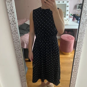 Svart prickig klänning Mint & Berry - Svart ärmlös klänning från Mint & Berry med vita prickar och resår i midjan. Klänningen har en öppen detalj i ryggen med knappstängning upptill. Storlek 40. Jag har storlek S i vanliga fall och så här sitter klänningen på mig. 
