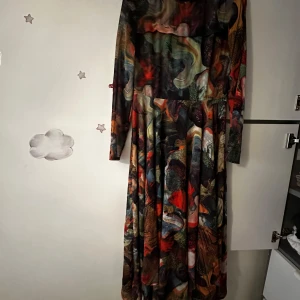 Mönstrad långklänning från Weekday - Säljer en långklänning från Weekday med färgstarkt abstrakt mönster i grönt, rött, orange och svart. Klänningen har lång ärm och rund halsringning. Perfekt för dig som gillar unika plagg med mycket färg och karaktär.