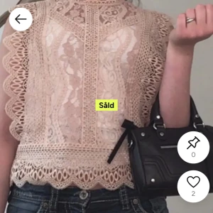 Beige spetsblus med volangdetaljer - Superfin beige blus i spets med vackra broderade detaljer och volangkant längs ärmar och nederkant. Blusen är ärmlös och har hög hals, perfekt för dig som gillar romantisk och söt stil. Snygg att matcha med jeans eller kjol.