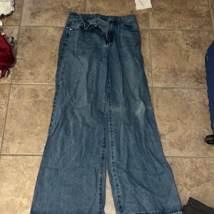 Blåa wide jeans med hög midja - Säljer ett par blåa jeans med riktigt breda ben och hög midja. Klassisk femficksmodell med dragkedja och knapp framtill. Perfekta för dig som gillar en avslappnad och trendig look.