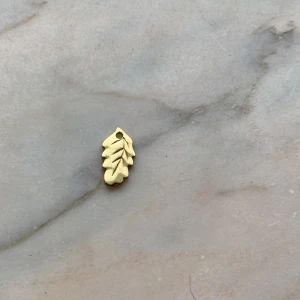 Guldigt Ekblads hänge från Ioaku - Litet hänge i form av ett ekblad från ioaku, hänget är guldplaterat perfekt som detalj till halsband eller armband. Bladet har fina ingraverade ådror och ett hål för att enkelt kunna fästas på en kedja.