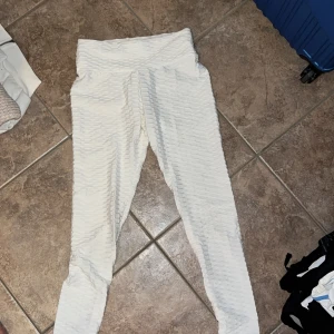 Vita scrunch leggings från SHEIN - Vita leggings från SHEIN i storlek S med scrunch-detalj bak och hög midja. De har en strukturerad, ribbad yta och är gjorda i stretchigt syntetmaterial som sitter tight och formar sig efter kroppen. Perfekta för träning eller chill.