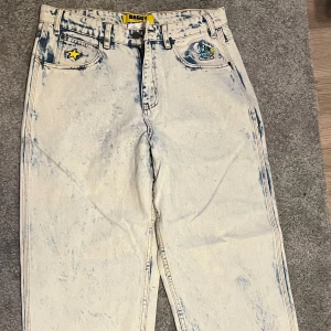 Baggy ljusa butter goods jeans - Baggy jeans i ljusblå blekt tvättad denim med coola tryck av stjärnor, noter och smurfar. Hög midja och raka ben. Flera broderade detaljer och patchar på fickorna, samt tydlig streetwear-vibe. Perfekta för dig som gillar statement-plagg. Ändast använda 2 gånger så skicket är riktigt bra!