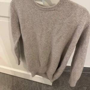 Beige Kashmir tröja med rund hals - En stilren beige kashmir tröja med rund halsringning och långa ärmar. Tröjan har en mjuk och skön känsla, perfekt för lager på lager. Passar dig som gillar en enkel och klassisk look med en neutral färgton.