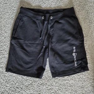 Sail Racing shorts - Svarta shorts från Sail Racing med snörning i midjan och tryckt logga på ena benet. Mjukt material och bekväm passform, med fickor fram och en bakficka. Perfekta för sommaren.
