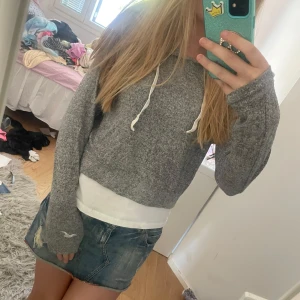 Grå hoodie från Hollister - Säljer en grå hoodie från Hollister med vit dragsko i huvan. Tröjan är mjuk och har långa ärmar, perfekt för en avslappnad stil. Passar dig som gillar en lite kortare modell.