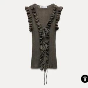 Olivgrön ribbad linnetopp med volang från Zara - Trendig olivgrön linnetopp från Zara med djup v-ringning, volangdetaljer längs axlar och framkant samt knyt framtill. Ribbad struktur och ärmlös design ger en cool och modern look.