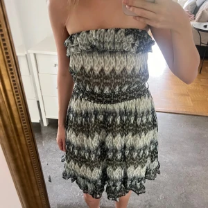  axelbandslös klänning med volanger - Säljer en axelbandslös kortklänning i mönster med volang upptill och smock i midjan. 