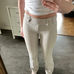 Beige kostymbyxor med vita ränder - Snygga beige kostymbyxor med vita vertikala ränder och låg midja. Byxorna har bootcut och stängs med både knapp och dragkedja framtill💕