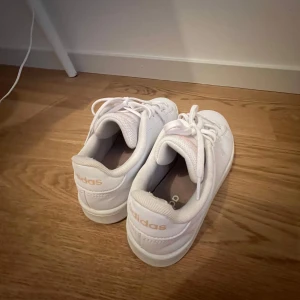 Vita adidas sneakers med rosa detaljer - Fräscha vita adidas sneakers med ljusrosa logga på plös och häl som jag inte har använt mycket och nu är de tyvärr för små för mig💕