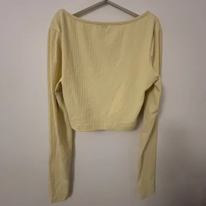 Ljusgul ribbad croppad topp - Superfin ljusgul croppad topp från shein med lång ärm och bred, rundad urringning. Toppen är ribbad och har en tight passform som sitter snyggt på kroppen. Perfekt att styla med jeans eller kjol för en fräsch look.