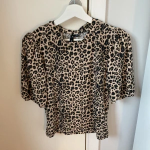 Leopardmönstrad topp med puffärm XS - Snygg topp från lager 157 i leopardmönster med beige och svarta toner. Modellen har puffiga korta ärmar och rund halsringning. Materialet är mjukt och stretchigt, perfekt för dig som vill sticka ut lite extra.