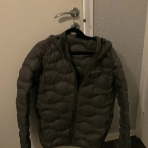 Grå dunjacka med huva från Peak Performance - Säljer en grå dunjacka från Peak Performance med huva och dragkedja framtill. Jackan är i princip helt oanvänd (någon enstaka gång). Nytt pris för denna ligger ute för mellan 2000-3000.