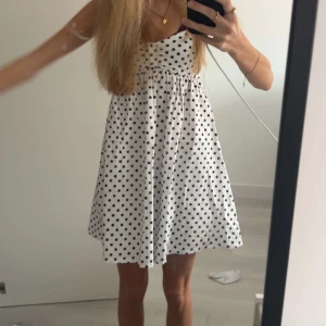 Vit prickig sommarklänning med smala axelband - Säljer en söt vit klänning med svarta prickar från zara. Klänningen har smala axelband, v-ringning och en lätt utställd kjol. Perfekt för varma dagar och har en luftig passform.