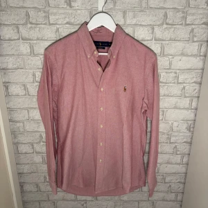Ralph Lauren skjorta - Rosa skjorta från Ralph Lauren i bomull med button down-krage och broderad logga på bröstet. Perfekt sommarplagg för stilrena outfits. Skjortan är i nyskick, inga tecken på användning! Hör av dig vid intresse 🙌