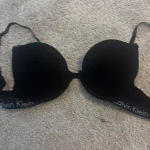 Svart bh från Calvin Klein - Säljer en svart bh från Calvin Klein med vadderade kupor och justerbara axelband. Bh:n har logotypen tryckt på resåren och ger ett stilrent och sportigt intryck. Knappt använd. Storlek 70 C!