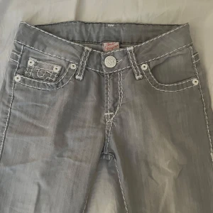 Ljus Grå True Religion jeans - längden passar perfekt på någon som är runt160-164 💕, Säljer ett par jätte snygga jeans från True Religion som är low waist  med tydliga vita kontrastsömmar och klassiska bakfickor med broderad logga. 