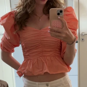 Korall puffärmad blus - Supersöt blus i korall med puffiga trekvartsärmar och volang nertill. Toppen har rynkade detaljer framtill och en croppad passform som ger en trendig look.  Blusen är från zara 