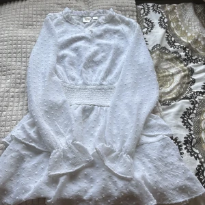 Vit volangklänning från Gina Tricot - Superfin vit klänning från Gina Tricot med volangdetaljer och strukturmönster. Klänningen har lång ärm, markerad midja med smock och volangkant vid halsen. Perfekt för sommarens tillfällen!katt finns i hemmet💕💕