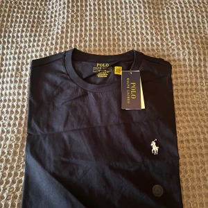 Svart t-shirt från Polo Ralph Lauren - Svart t-shirt från Polo Ralph Lauren med klassisk vit broderad logga på bröstet. Modellen är custom slim fit och har rund halsringning. Perfekt för dig som gillar stilrena och tidlösa plagg. Är öppen för förhandling.