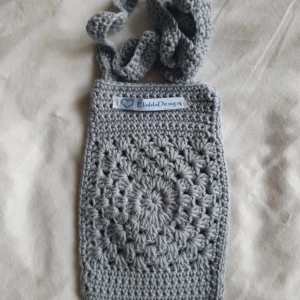 Grå virkad axelväska från ElindaDesign - Säljer en handgjord grå virkad axelväska från ElindaDesign. Väskan har ett unikt mönster framtill och en bred, virkad axelrem. Perfekt för att bära småsaker och ge din outfit en personlig touch. Väskan är ca 18 x 12 cm. Perfekt till mobilen.