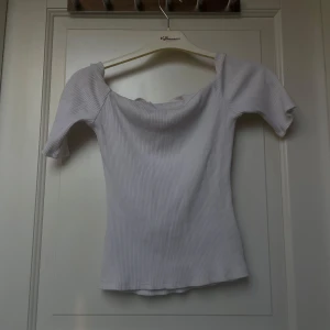 Vit ribbad topp från H&M - Säljer en vit ribbad topp från H&M med korta puffärmar och en lätt rynkad, vid halsringning. Toppen är figurnära och har en mjuk, stretchig känsla. Perfekt för en stilren och enkel look.