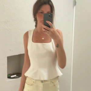 Artitzia Vit linnetopp med volangkant - Säljer en stilren vit linnetopp från Aritzia med fyrkantig ringning och volangkant nedtill. Toppen är ärmlös och har en figurnära passform som ger en snygg siluett. Använt en gång!