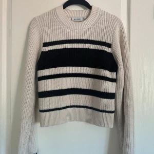 Randig stickad tröja från Weekday - Säljer en stickad tröja från Weekday i beige med svarta ränder. Tröjan har rund halsringning och långa ärmar. Materialet består av 55% polyester och 45% bomull. Perfekt för lager-på-lager och en stilren vardagslook.