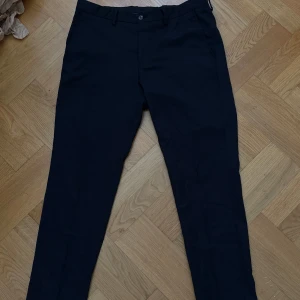 Svarta kostymbyxor med normal passform - Snygga svarta kostymbyxor med klassisk rak passform och diskreta fickor bak. Perfekta till skjorta eller stickad tröja. Stängs med knapp och dragkedja framtill.