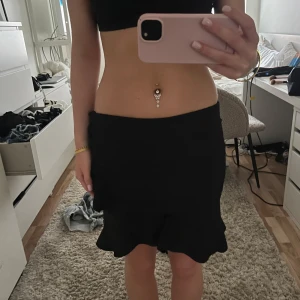 Svart volangkjol från Nelly  - Säljer en svart kortkjol från NLY med volangdetalj längs nederkanten och omlottkänsla i designen. Kjolen har en feminin och trendig look, perfekt att styla med en crop top eller blus. Materialet känns mjukt och följsamt. Stretchigt material, skit söt !!💕💕