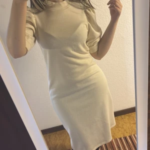 Beige klänning med puffärmar - Säljer en stilren beige klänning med puffiga kortärmar och rund halsringning. Modellen är rak och går till knäna, vilket ger en klassisk och enkel look. Perfekt för dig som gillar minimalistisk stil och mjuka färger.
