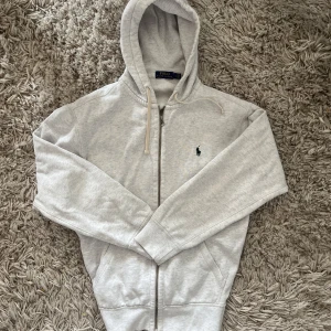 Ljusgrå hoodie från Polo Ralph Lauren - Säljer den eftertraktade Ralph lauren koftan med den gamla modellen i storlek L. Använts lite grann men är som ny. Bud accepteras 😊