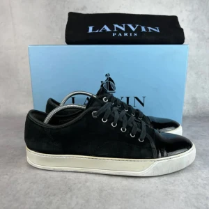 Lanvin  - Snygga svarta sneakers från Lanvin med ovandel i mocka och blanka lackdetaljer på tån och längs snörningen. Skorna har vita platta sulor och klassisk snörning. Perfekta för dig som vill ha en stilren och lyxig look.