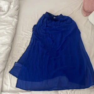 Blå långkjol med transparent lager - Säljer en blå lång kjol med ett snyggt transparent ytterlager. Klänningen har en enkel och flowy design som ger en luftig känsla. Perfekt för dig som gillar stilrena och eleganta plagg. Fodrad underklänning och lätt material.