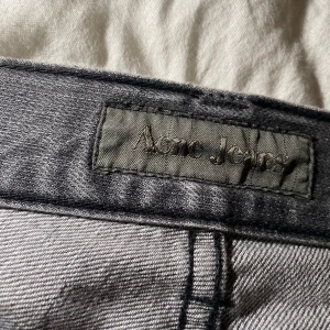 Grå jeans från Acne Jeans - Säljer ett par grå jeans från Acne Jeans i storlek 31/34 med klassisk femficksdesign och dragkedja. Jeansen har raka ben och normal passform, perfekta för en stilren vardagslook. Materialet är mjukt denim och färgen är en snygg, tvättad grå nyans.