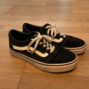 Svarta sneakers från Vans med vit sula - Klassiska svarta Vans sneakers med vit sula och vit sidosöm. Skorna har snörning och en platt sula, samt rund tå. Perfekta för en avslappnad och stilren look. 